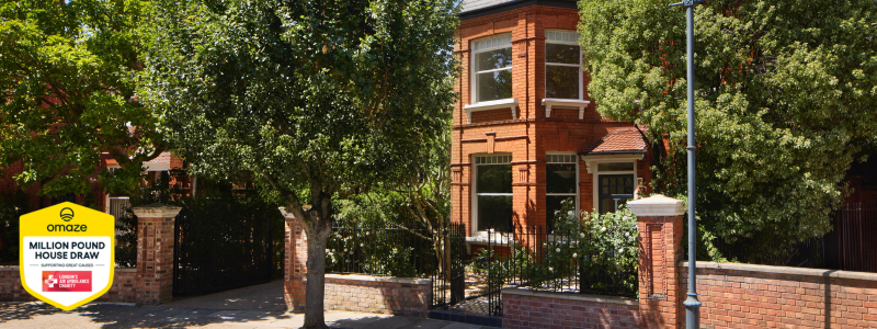 The exterior of the house, showing a leafy street in the sun and focussing on a beautiful double-fronted property with the Omaze x London's Air Ambulance Charity campaign shield in the corner