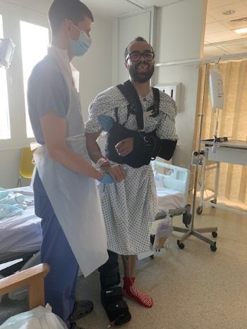 On standing up in hospital, wearing a back brace and a moon boot