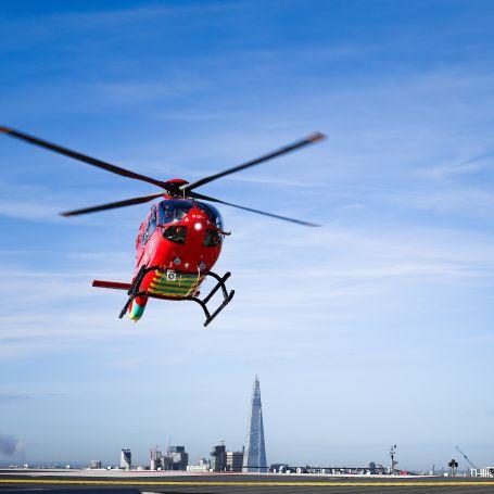 London's Air Ambulance helicopter landing on the helipad, with skyline of London in distance